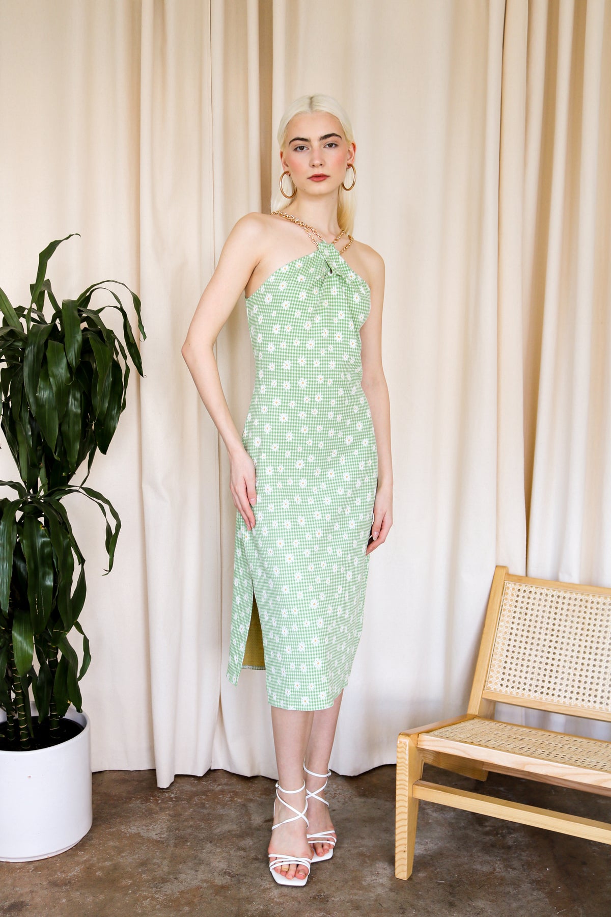 Model is wearing a green gingham midi dress with floral detail and criss cross gold chain detail around the neckline. Front facing.