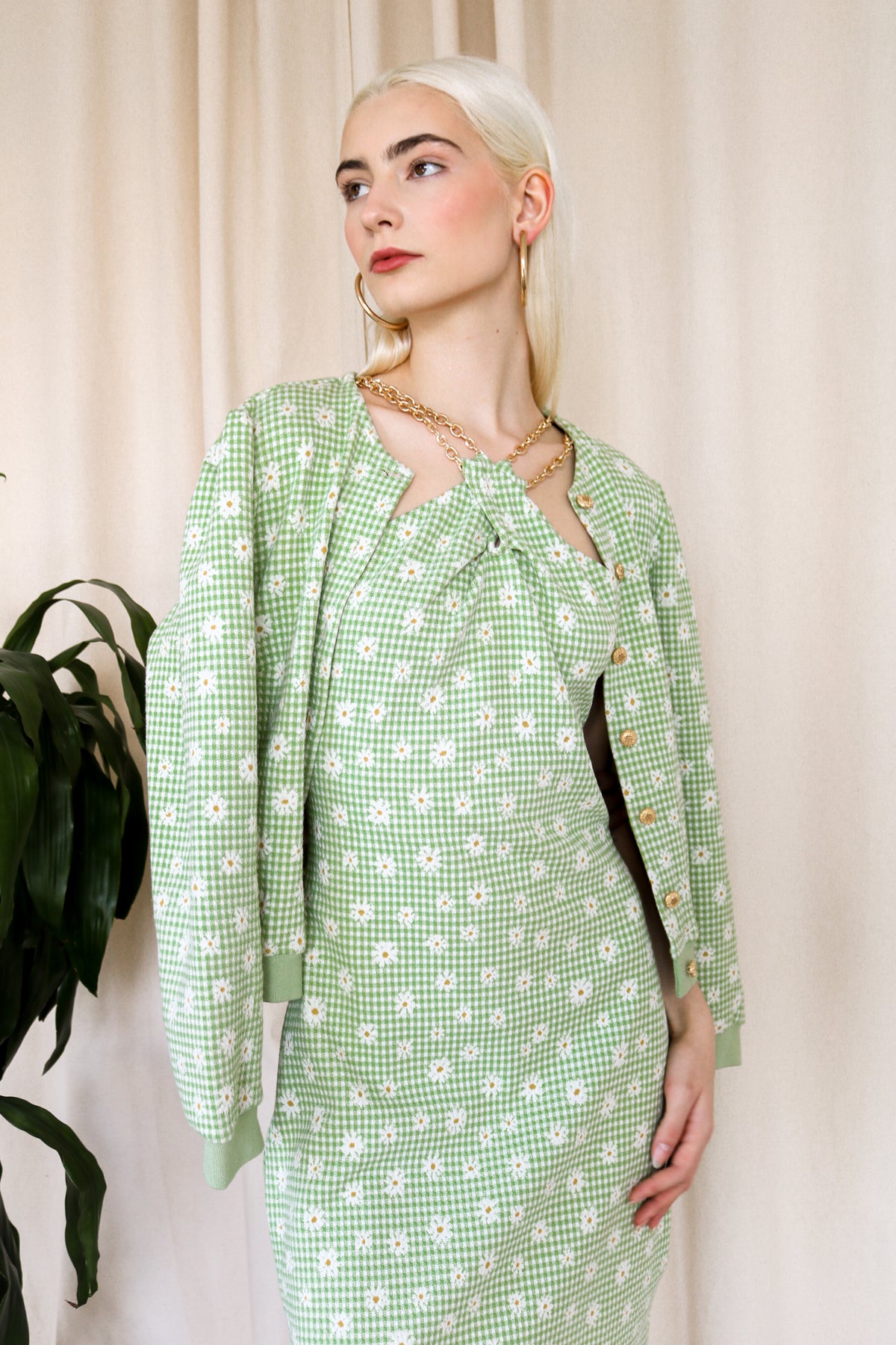 Model is wearing a green-plaid knitted cardigan with floral details. The cardigan includes gold metallic buttons. Front facing.