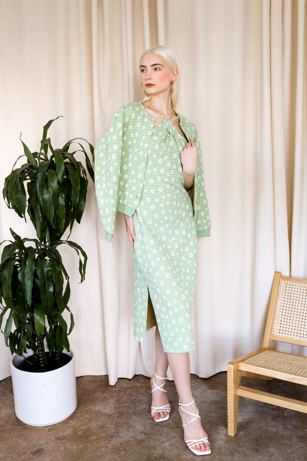 Model is wearing a green-plaid knitted cardigan with floral details. The cardigan includes gold metallic buttons. Model is also wearing white heels. Front facing.