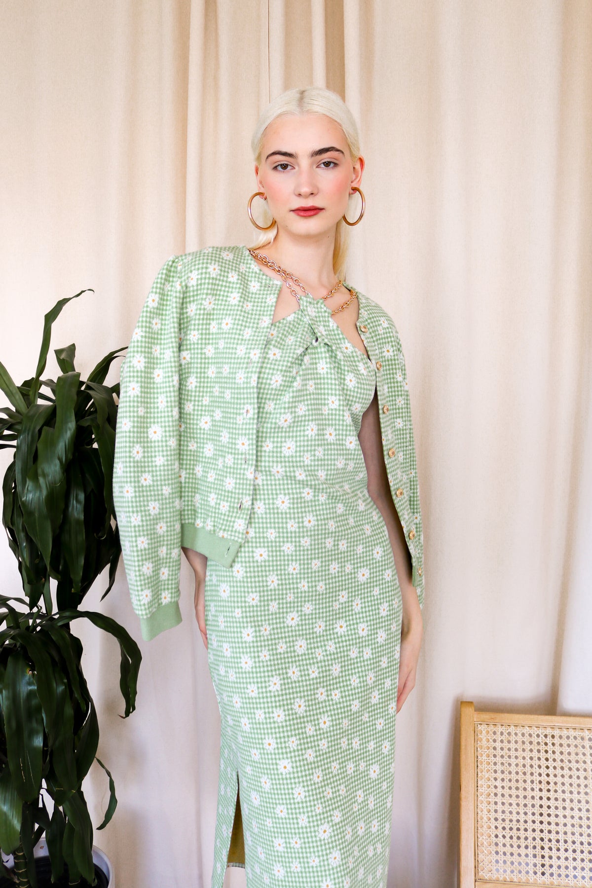 Model is wearing a green-plaid knitted cardigan with floral details. The cardigan includes gold metallic buttons. Front facing.