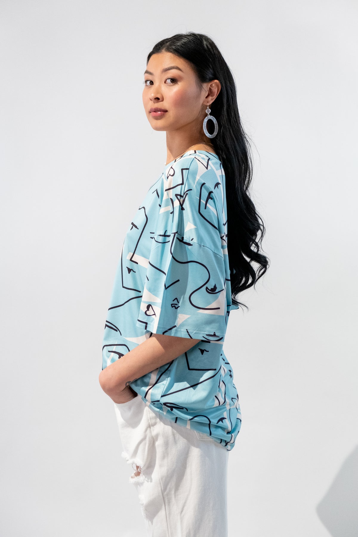 Model wearing a blue oversized t-shirt with an abstract faces graphic design