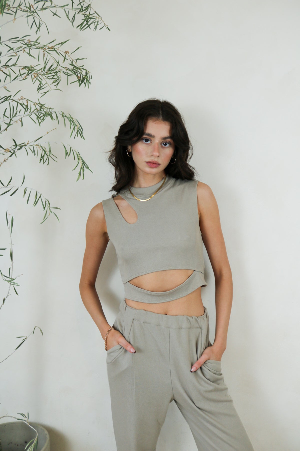 Model wears the sustainable sleeveless cut out crop top in the rosetta color. Standing in front of a white wall and facing the front.