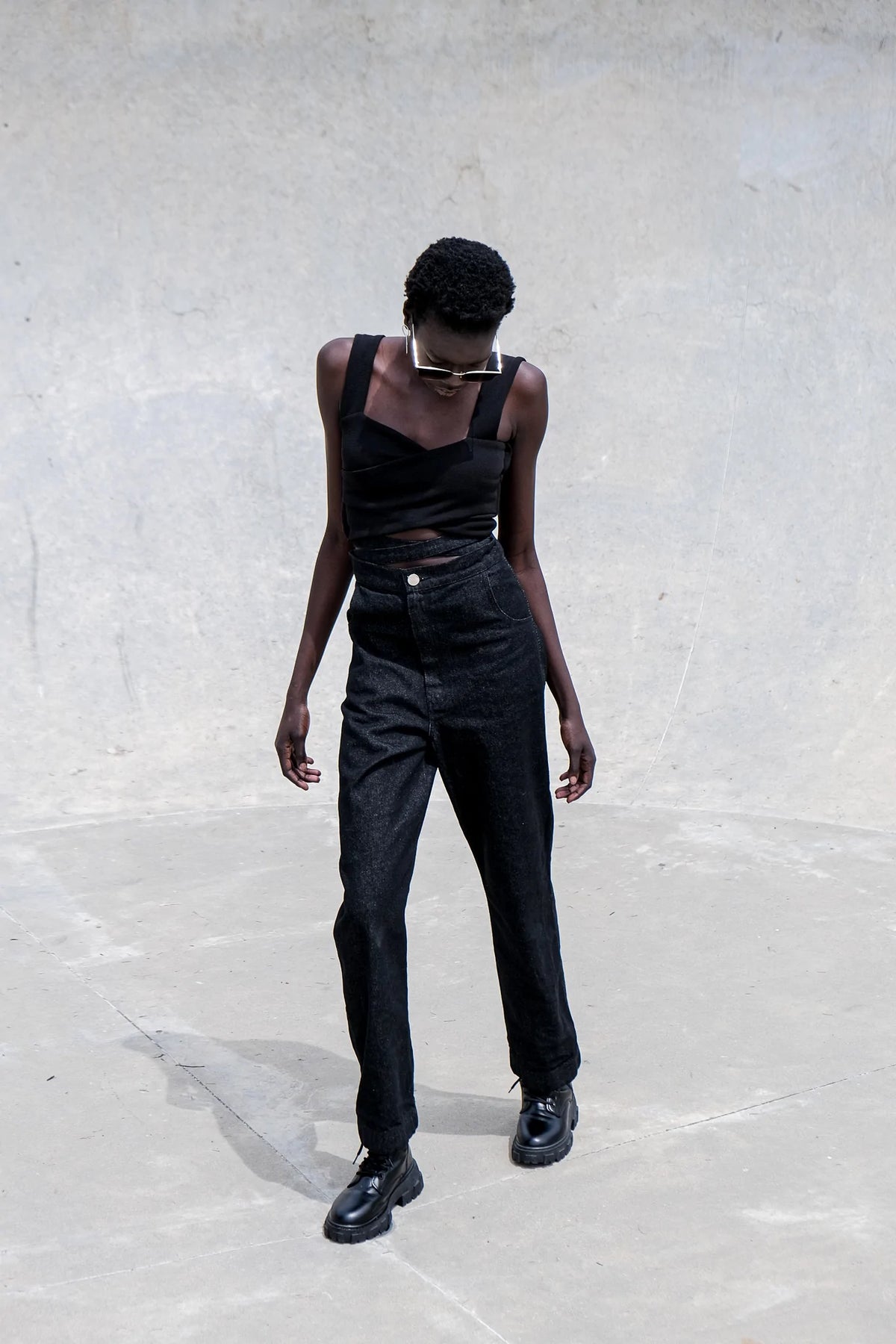 Model stands against minimal background outdoors wearing a sleeveless cross over knitted crop top in black..