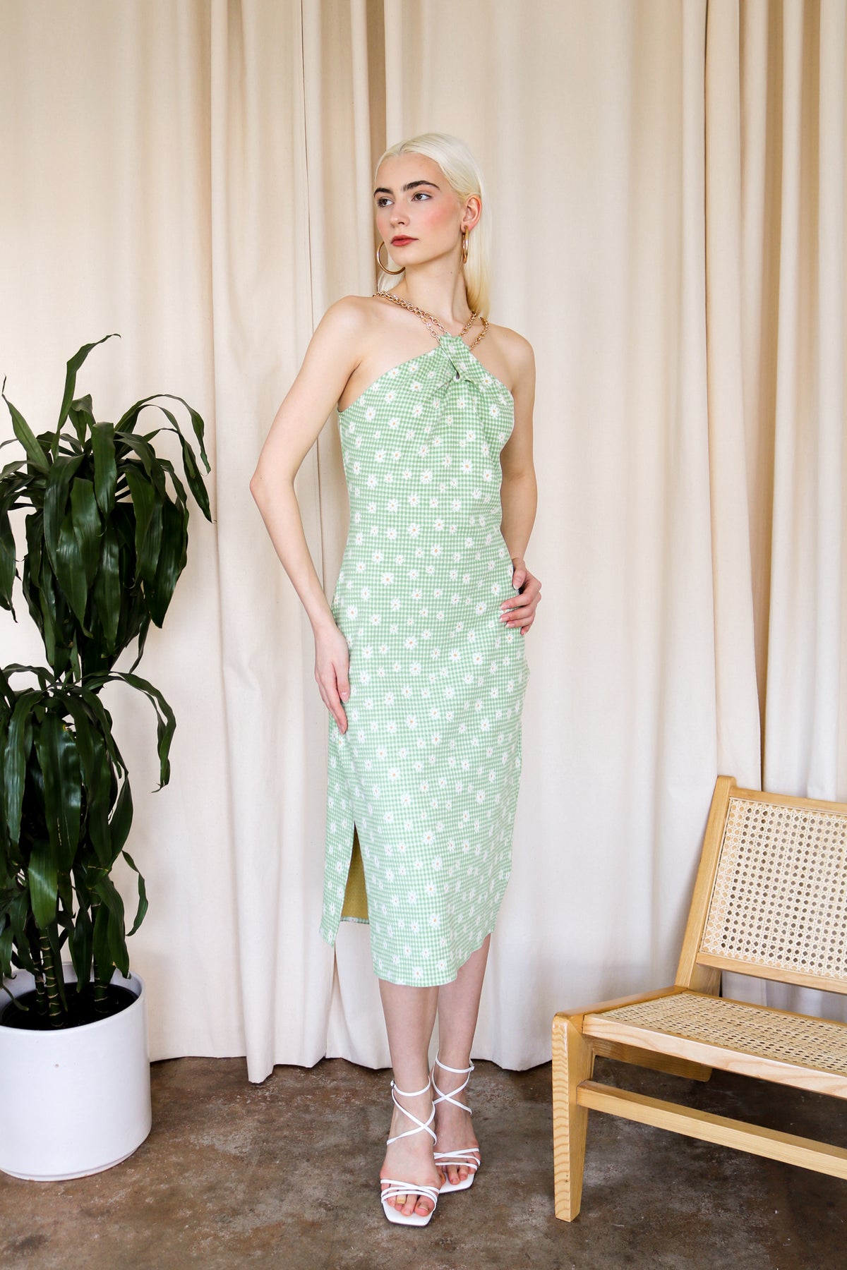 Model is wearing a green gingham midi dress with floral detail and criss cross gold chain detail around the neckline. Front facing. 