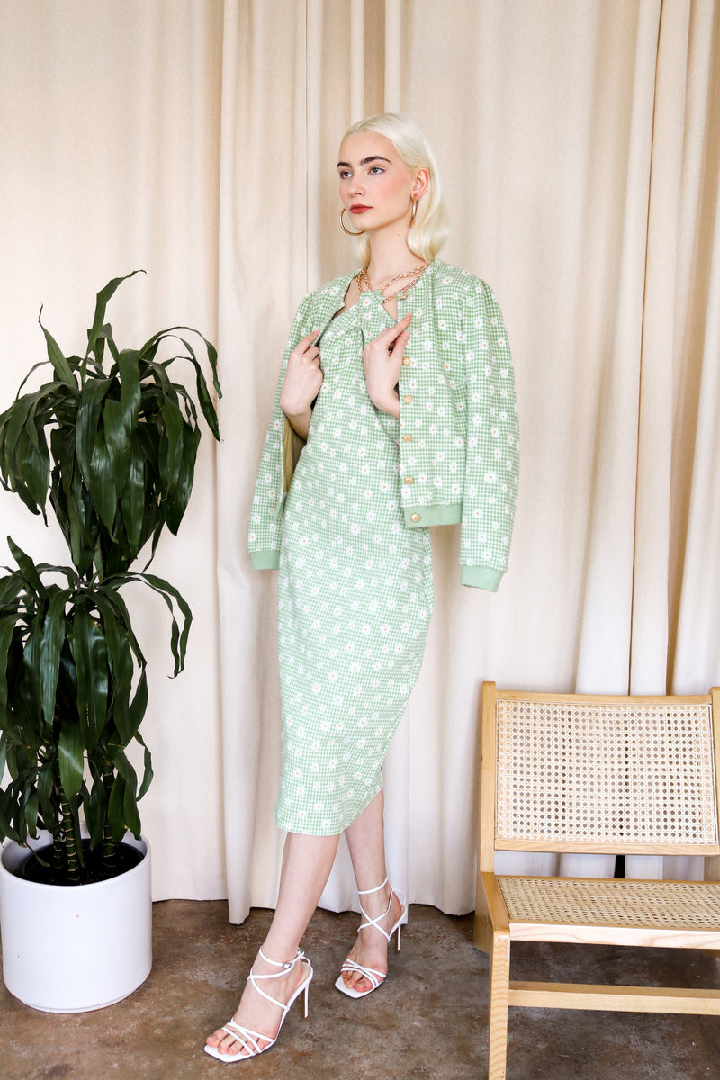 Model is wearing a green gingham midi dress with floral detail and criss cross gold chain detail around the neckline. Featuring matching cardigan. Front facing. 