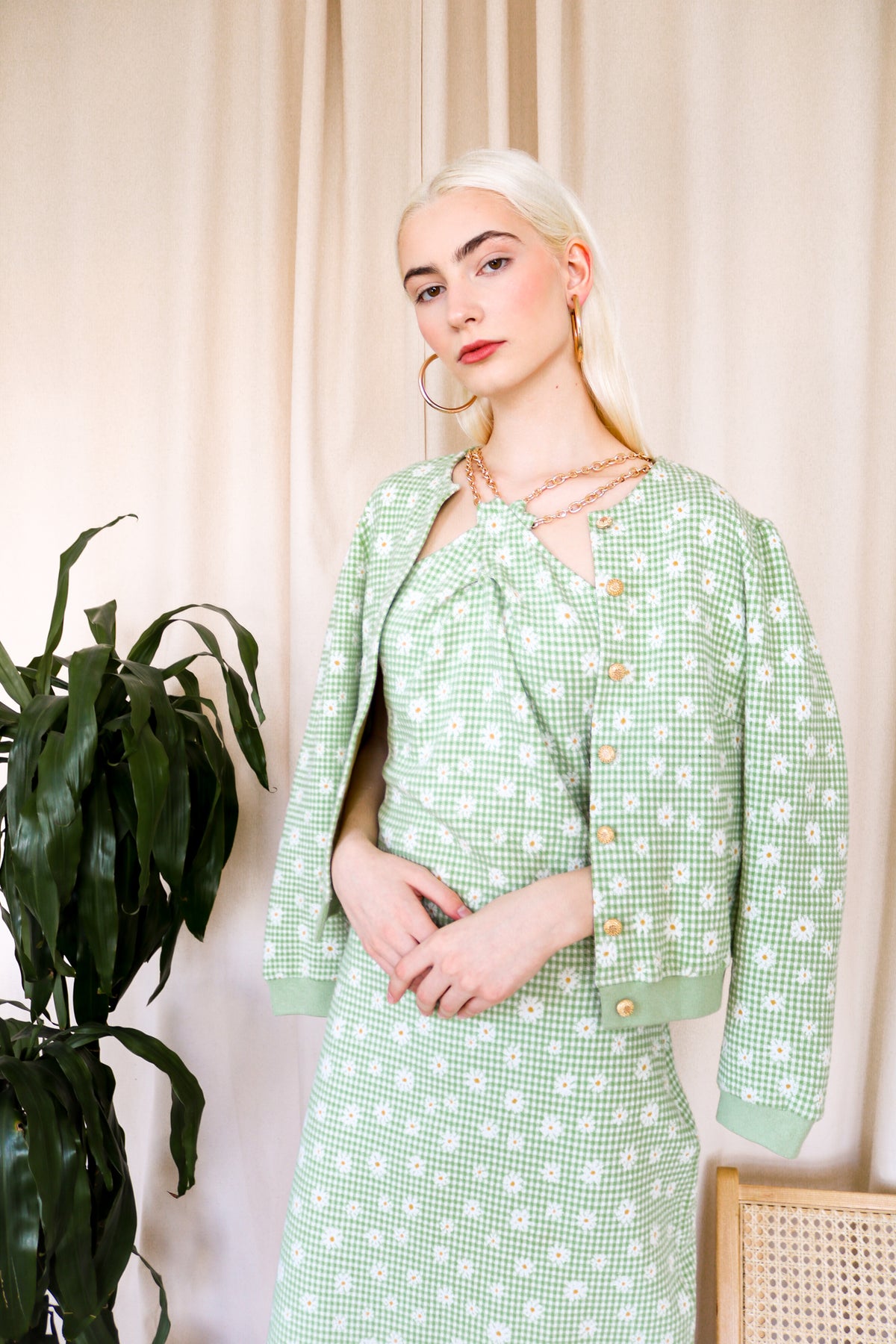 Model is wearing a green gingham midi dress with floral detail and criss cross gold chain detail around the neckline. Wearing matching cardigan.Front facing close up.