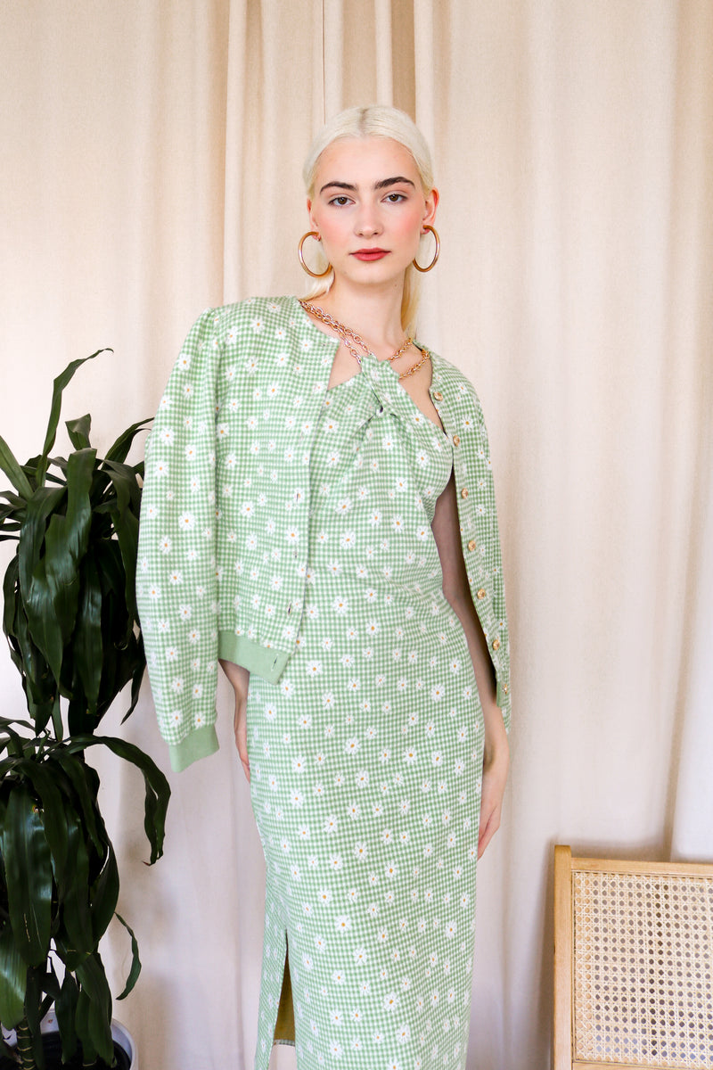 Model is wearing a green-plaid knitted cardigan with floral details. The cardigan includes gold metallic buttons. Front facing. 