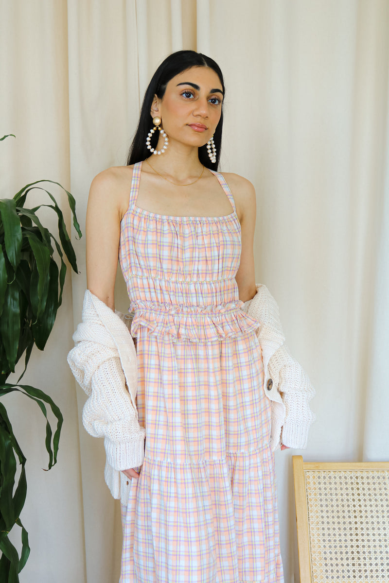 Model wearing a pink plaid smocked tiered maxi dress with a white cardigan,