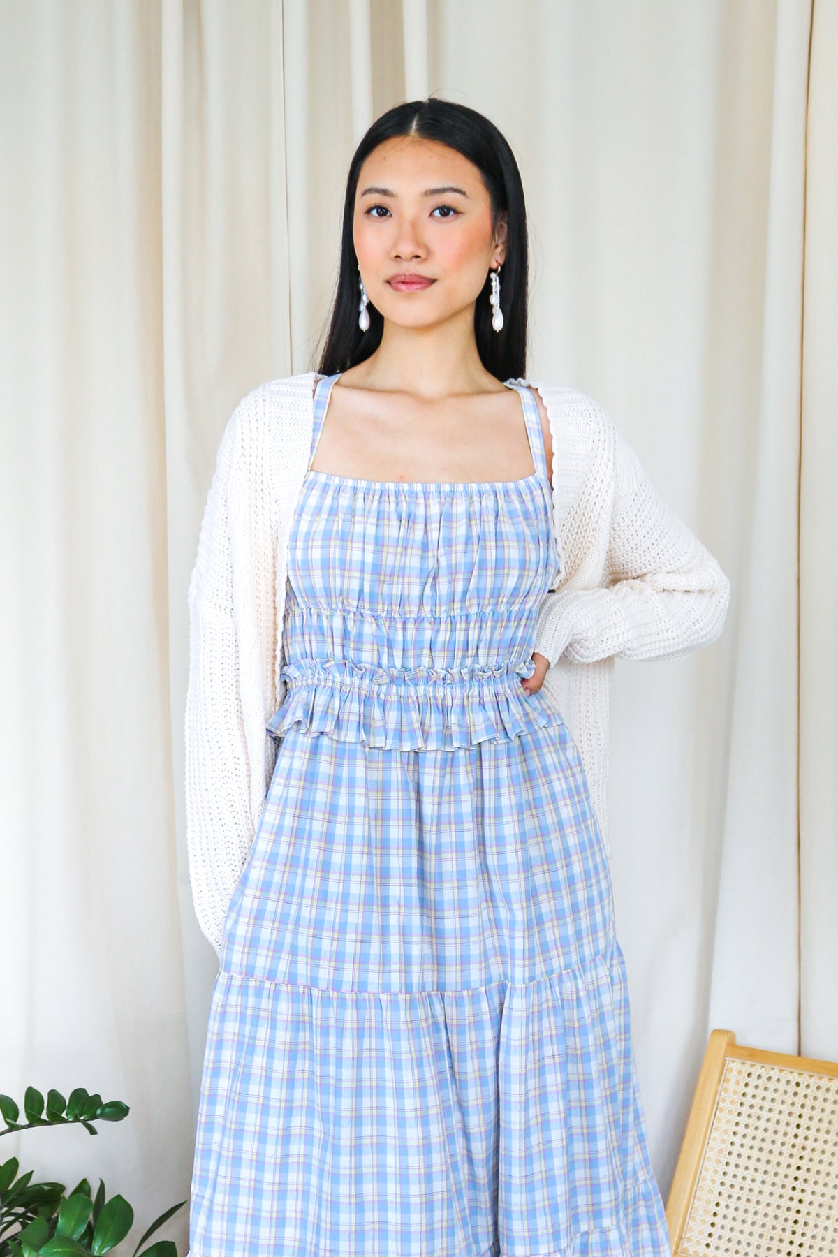 Model wearing a blue plaid smocked tiered maxi dress with a white cardigan.