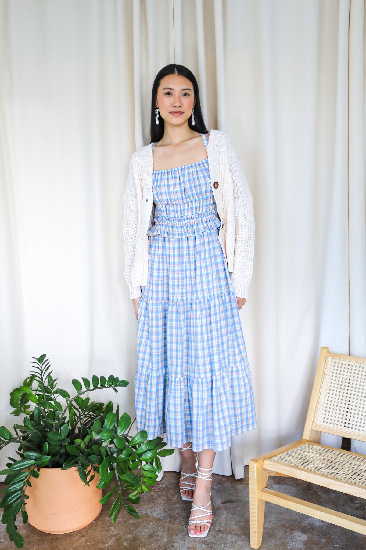 Model wearing a blue plaid smocked tiered maxi dress with a white cardigan
