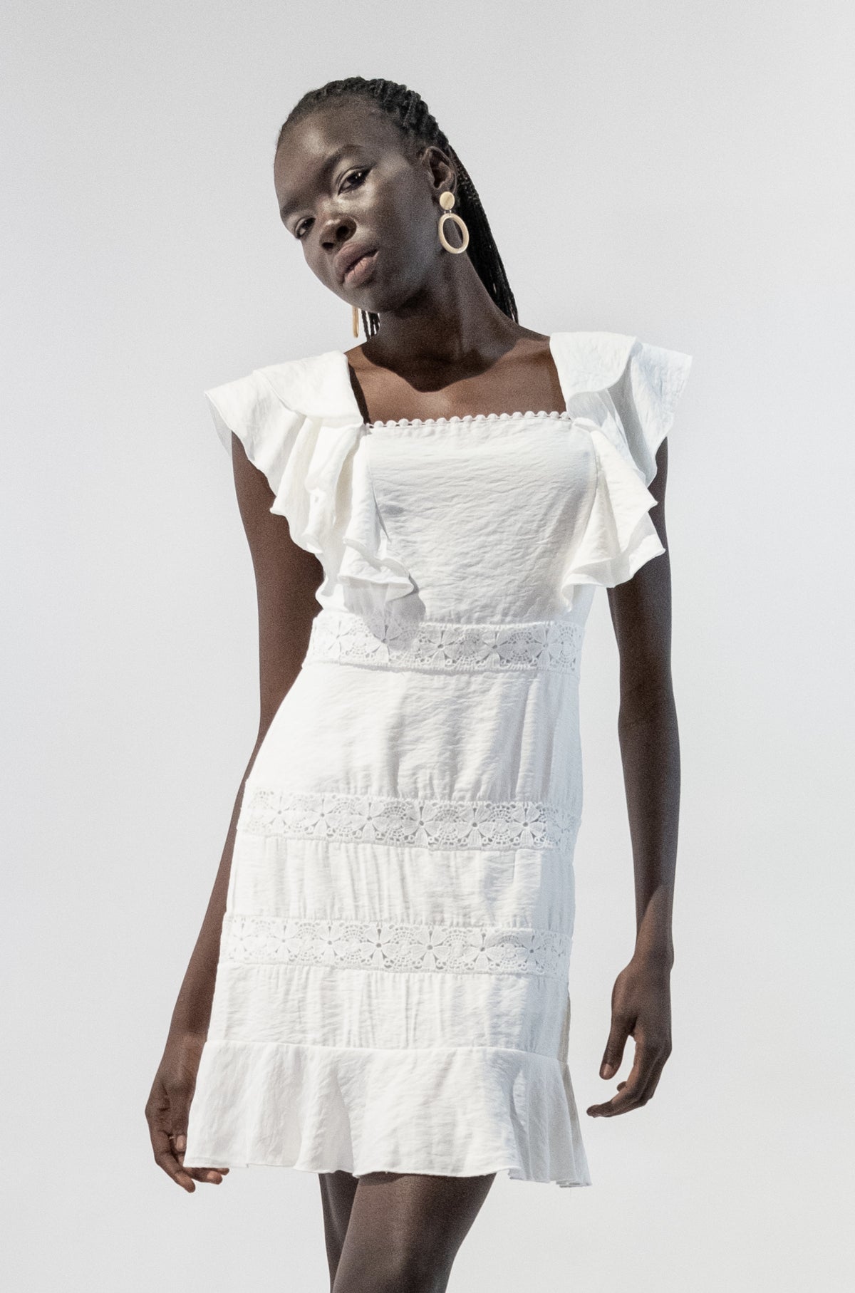 Model wearing white ruffle short sleeves lace dress with square neckline and floral detailing