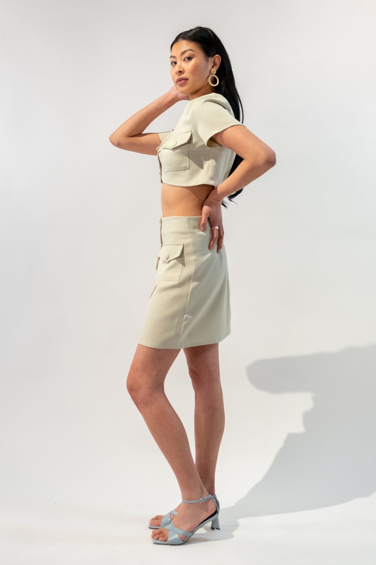 Model wearing a chic short sleeve button-up crop top and button skirt set in beige. Side.