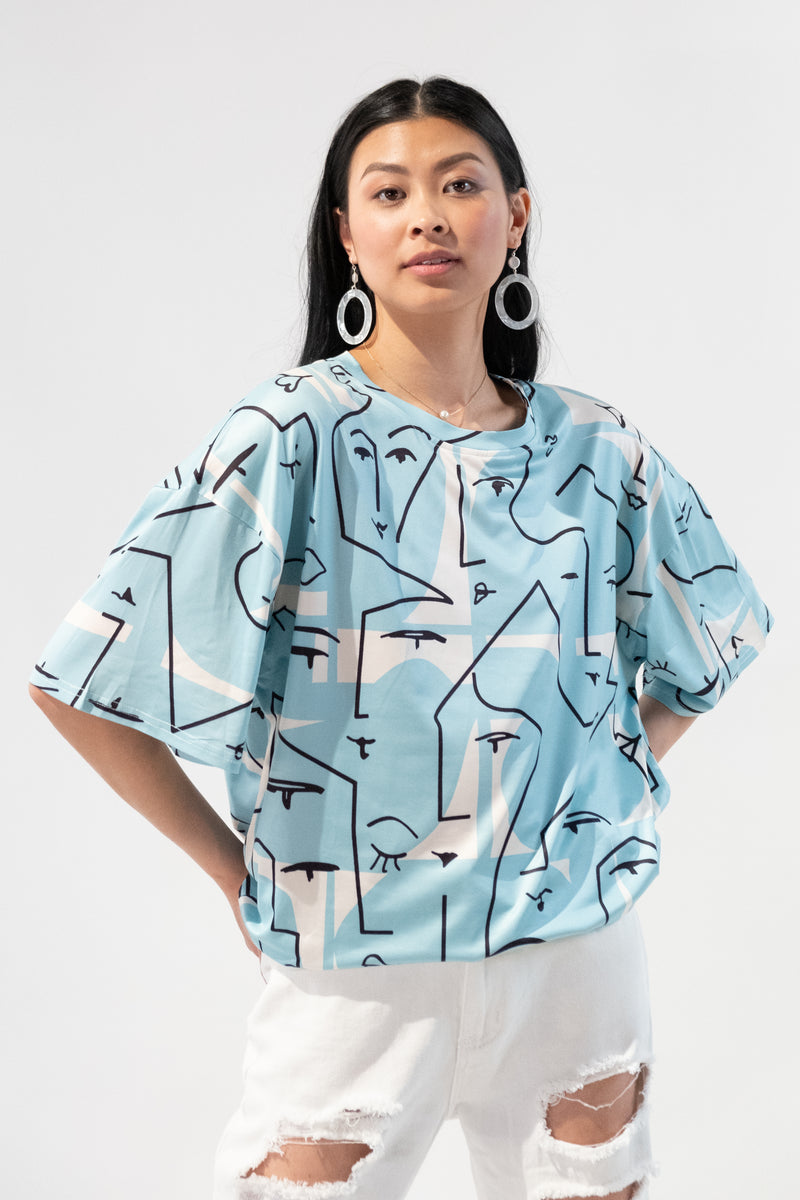 Model wearing a blue oversized t-shirt with an abstract faces graphic design