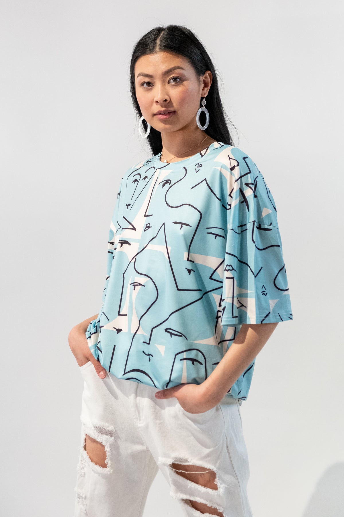 Model wearing a blue oversized t-shirt with an abstract faces graphic design