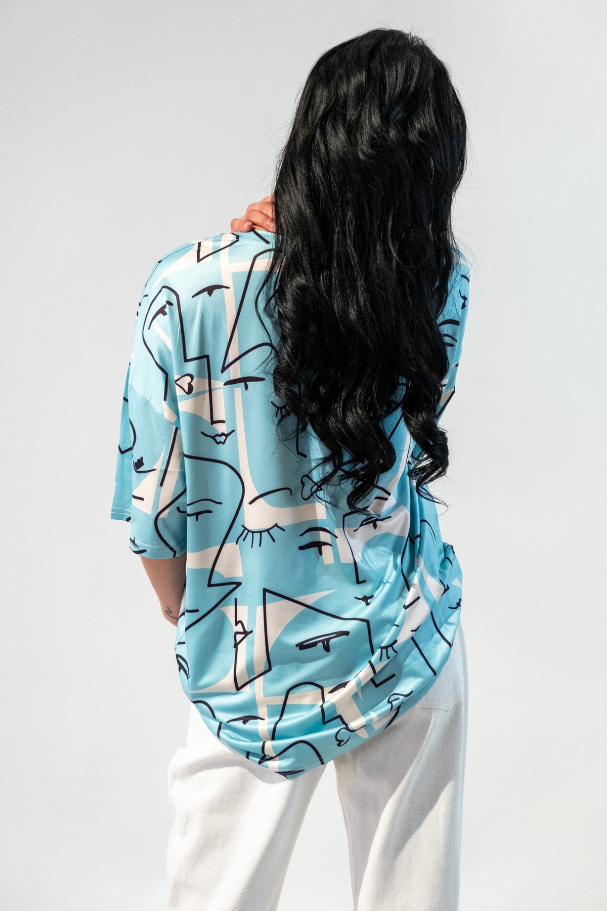 Model wearing a blue oversized t-shirt with an abstract faces graphic design. Back.
