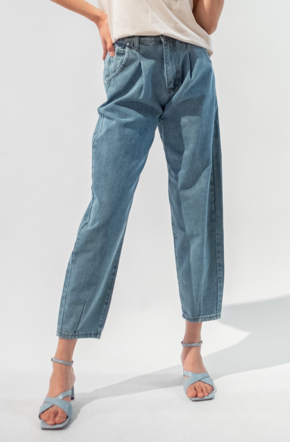 Model wearing the High Waisted Pleated Jeans with strappy blue heels. 