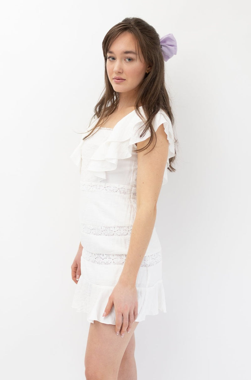 Model wearing white ruffle short sleeves lace dress with square neckline and floral detailing.
