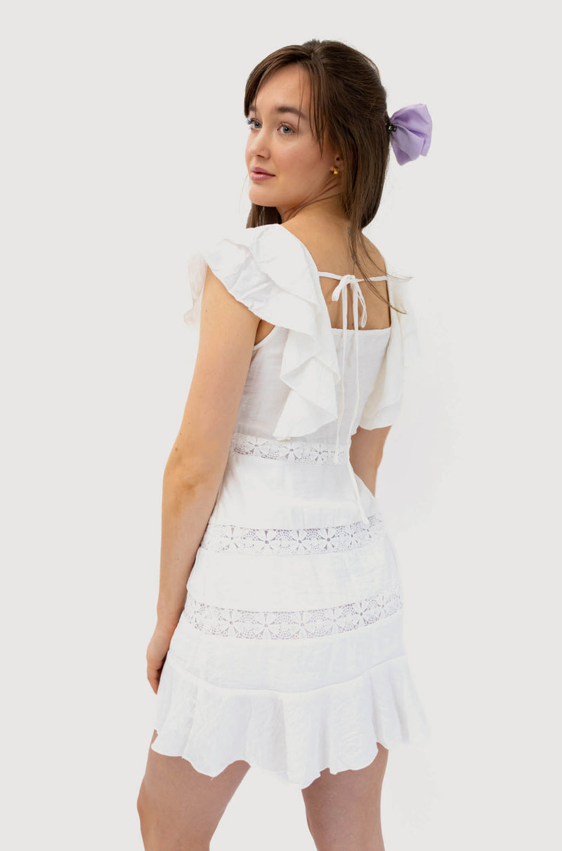 Model wearing white ruffle short sleeves lace dress with square neckline and floral detailing. Back side.