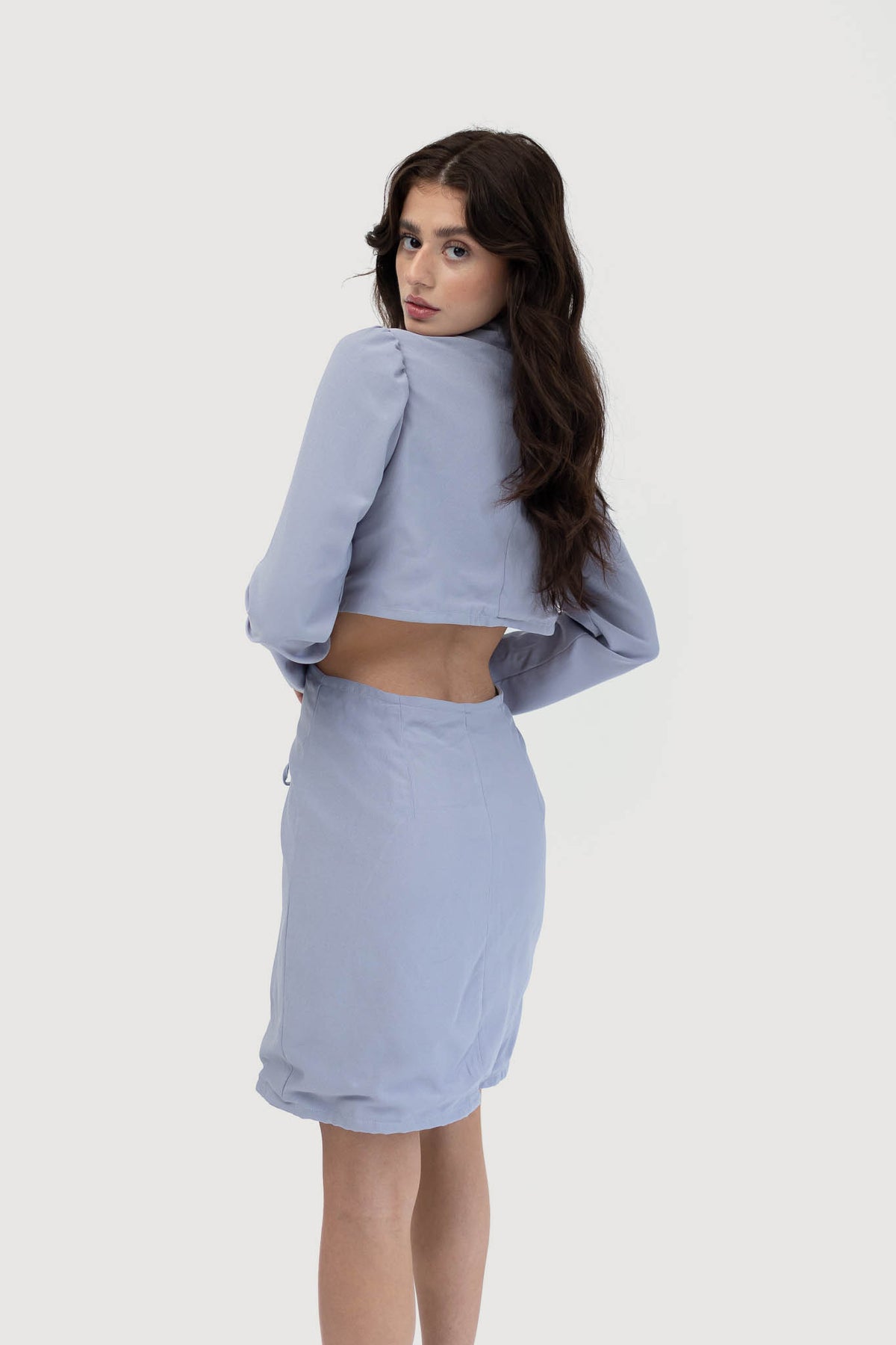 Model wearing an elegant Nepal blue dress with long sleeves, a structured collar, lace-up front detail, and side cut-outs. Showing back side cutout.
