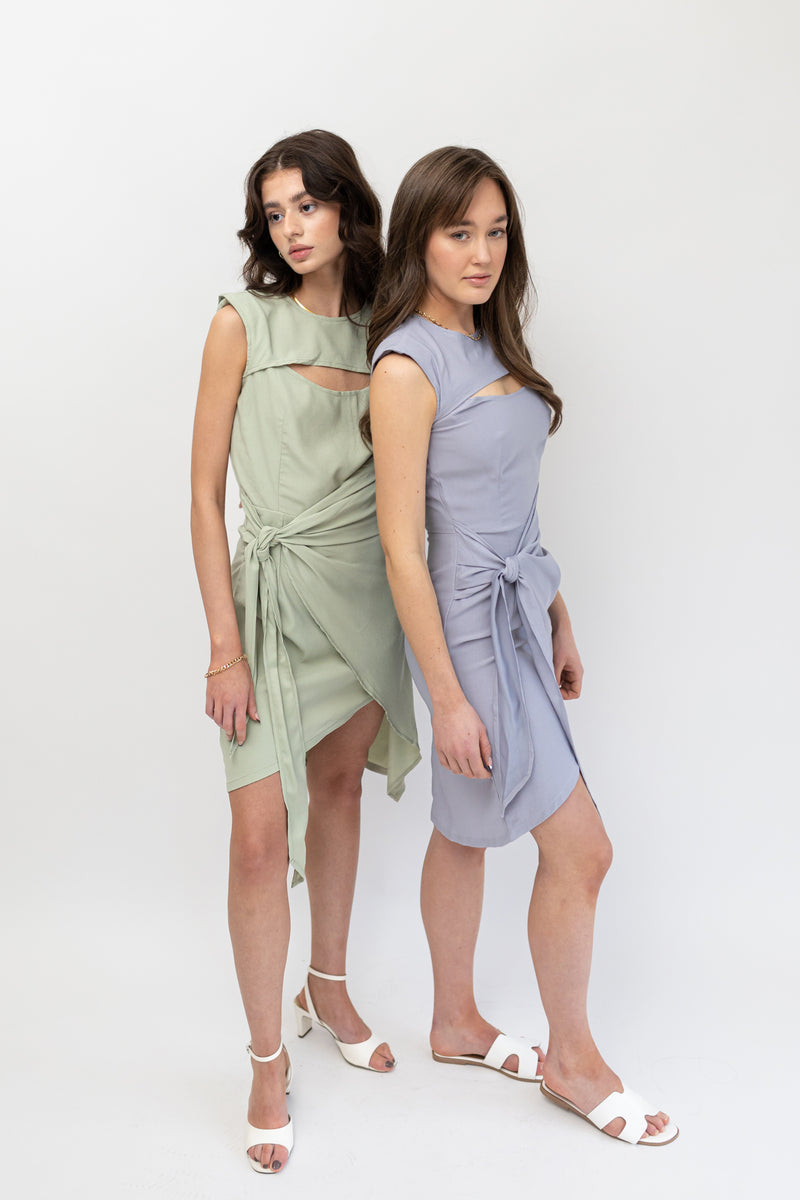 Two models showcasing elegant asymmetrical dresses in mint green and Nepal blue, featuring round necklines, crescent-shaped cutouts at the bust, and front tie details.