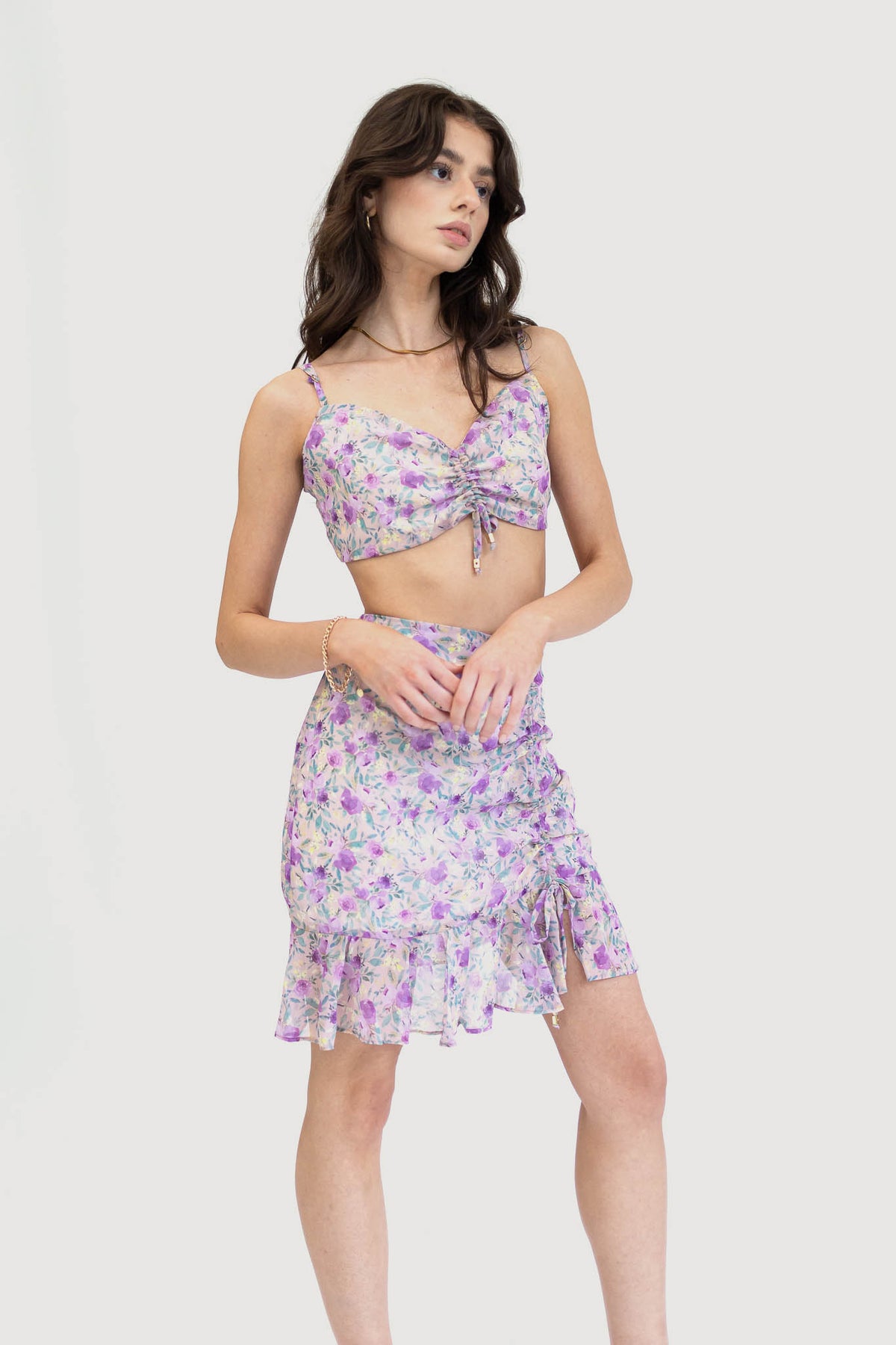 Model wearing a floral ruched crop top with adjustable spaghetti straps and a matching high-waisted skirt with a ruffled hem.